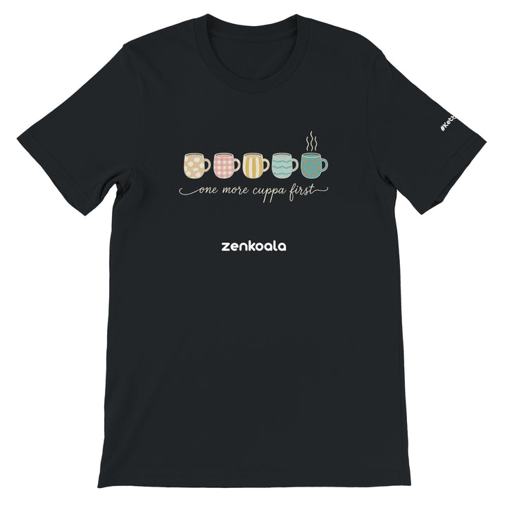 One More Cuppa First feel-good tee in black — five cosy patterned mugs, one still steaming, Zen Koala Australia